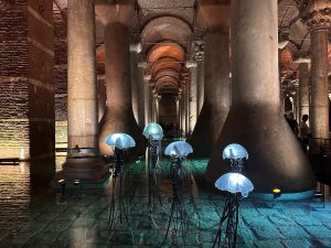An art exhibit features jellyfish sculptures in front of large pillars.