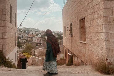 A Palestinian girl stands with her back to the camera looking down a city street