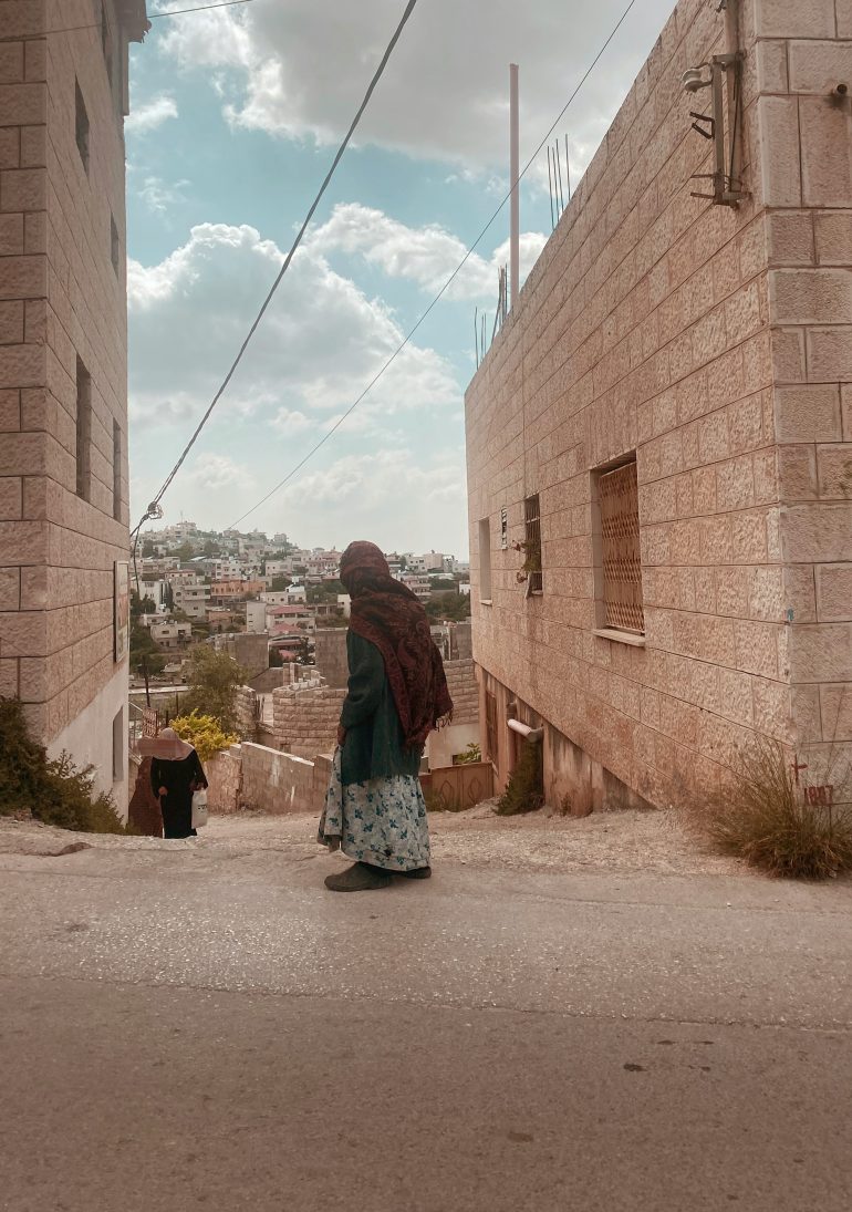 A Palestinian girl stands with her back to the camera looking down a city street