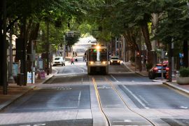 A MAX train drives down a tree-lined street